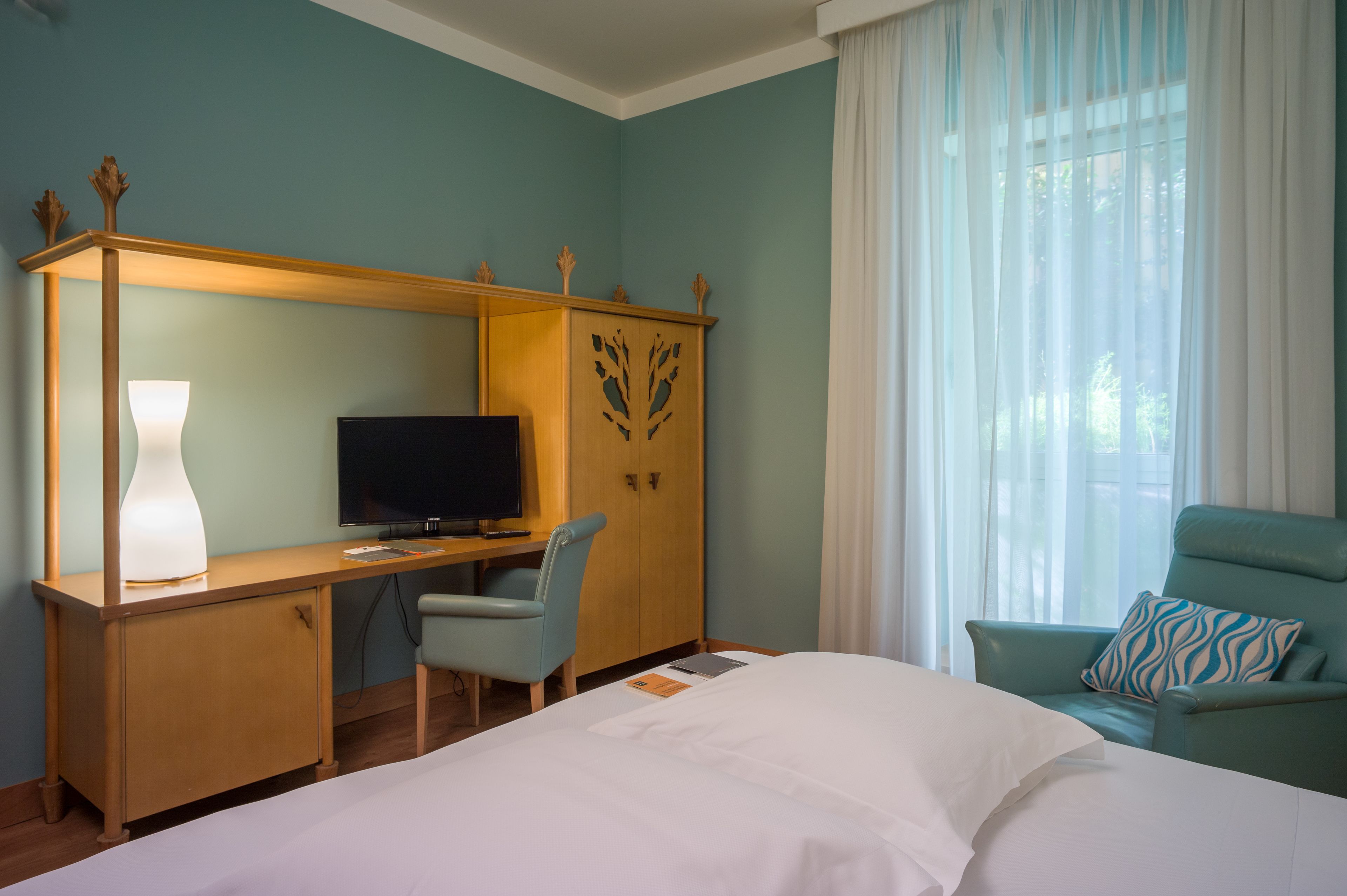 Habitación de hotel con cama, escritorio con ordenador, silla, televisor y armario.