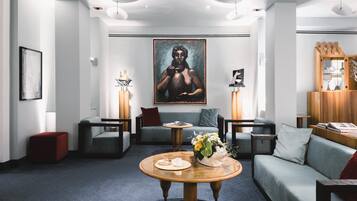 A modern hotel lobby with a central seating area, a large artwork on the wall, and a wooden coffee table with a vase of flowers.
