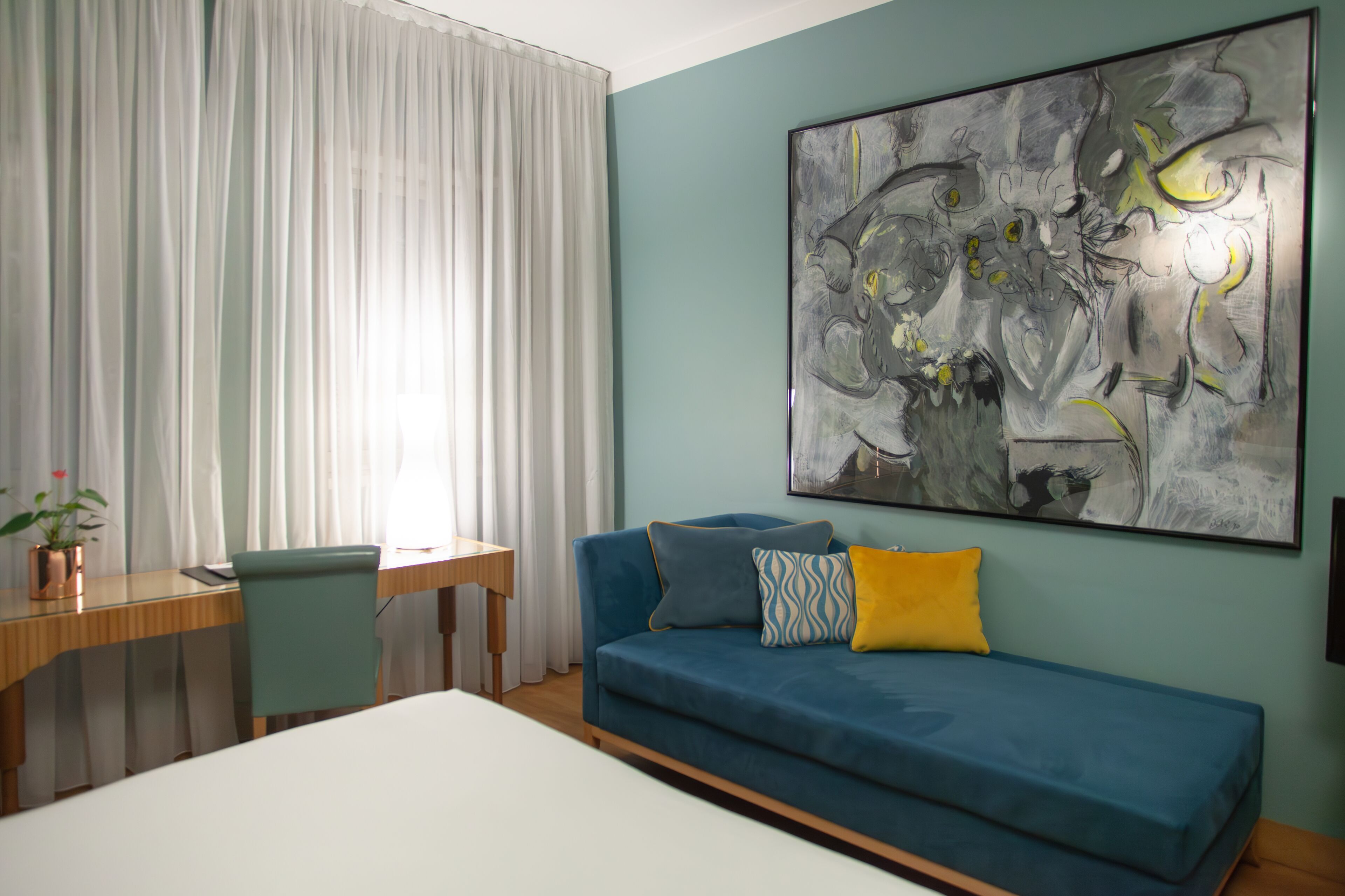 A room with a blue sofa, a desk, and a large abstract painting on the wall.