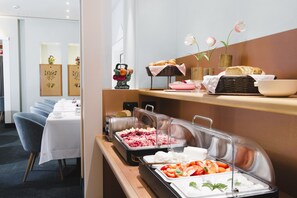 A buffet setup with various food items, a seating area with tables, and decorative elements like flowers and artwork. - Hotel Spadari Al Duomo (Milan)