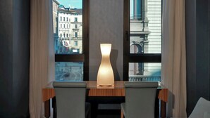 A modern hotel room with a wooden desk, two grey chairs, and a large window with a view of city buildings. - Hotel Spadari Al Duomo (Milan)