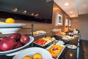 A buffet with various fruits and vegetables, a television, and framed pictures on the wall. - Crowne Plaza Boston - Woburn by IHG (Woburn)