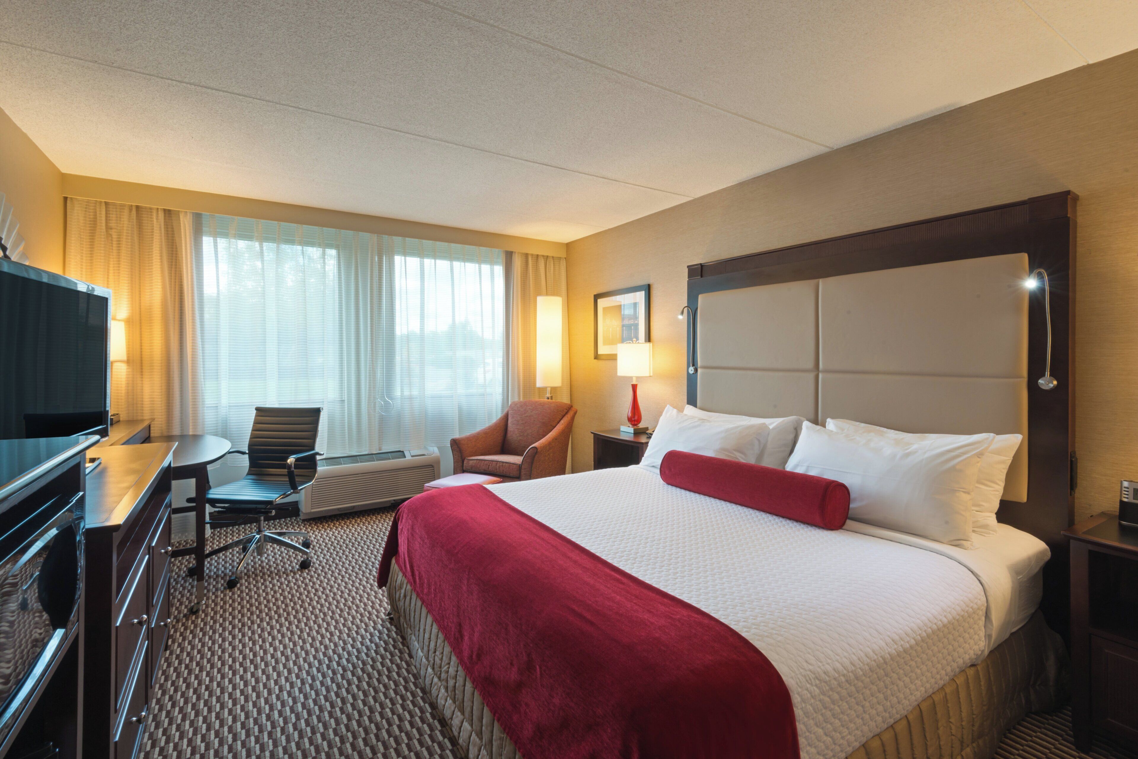 A hotel room with a bed, a desk, a chair, a TV, and a window with curtains.