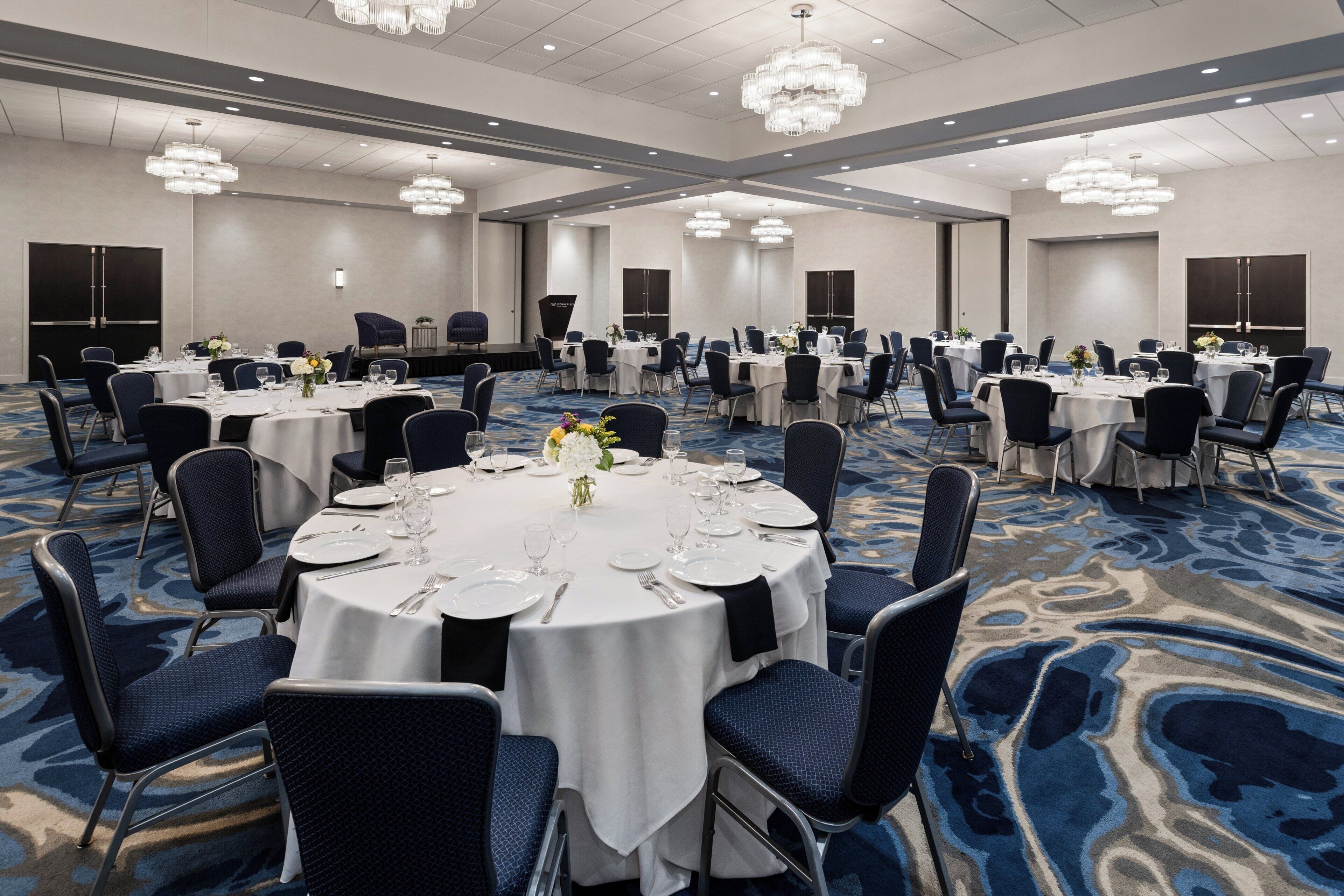 A large conference room with round tables, chairs, and chandeliers.