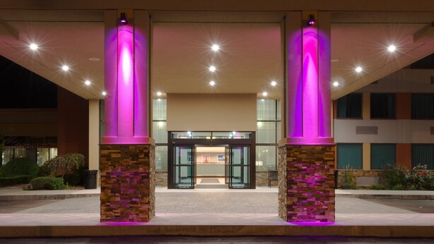 A hotel entrance with a glass door, illuminated pillars, and a paved walkway.
