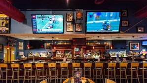 A bar with multiple screens displaying sports events, a variety of bottles, and a seating area with tables and chairs.