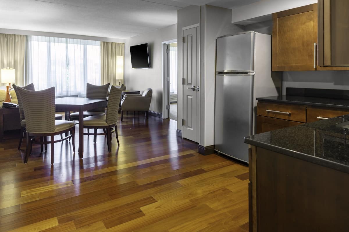 A hotel room with a dining area, a kitchen with a refrigerator, and a TV mounted on the wall.