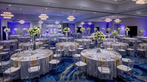 A banquet hall with round tables, clear chairs, and floral centerpieces.
