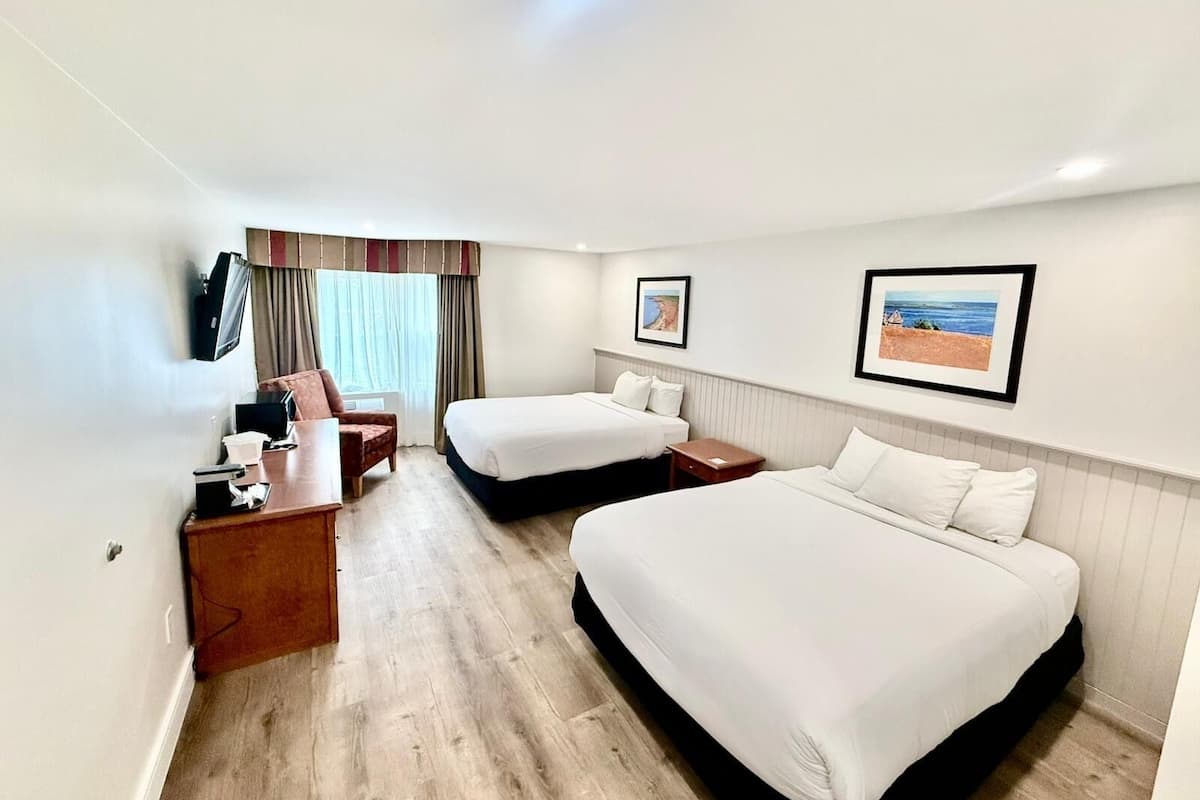 A hotel room with two beds, a desk, a chair, a TV, and framed pictures on the wall.
