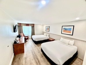 A hotel room with two beds, a desk, a chair, a TV, and framed pictures on the wall.