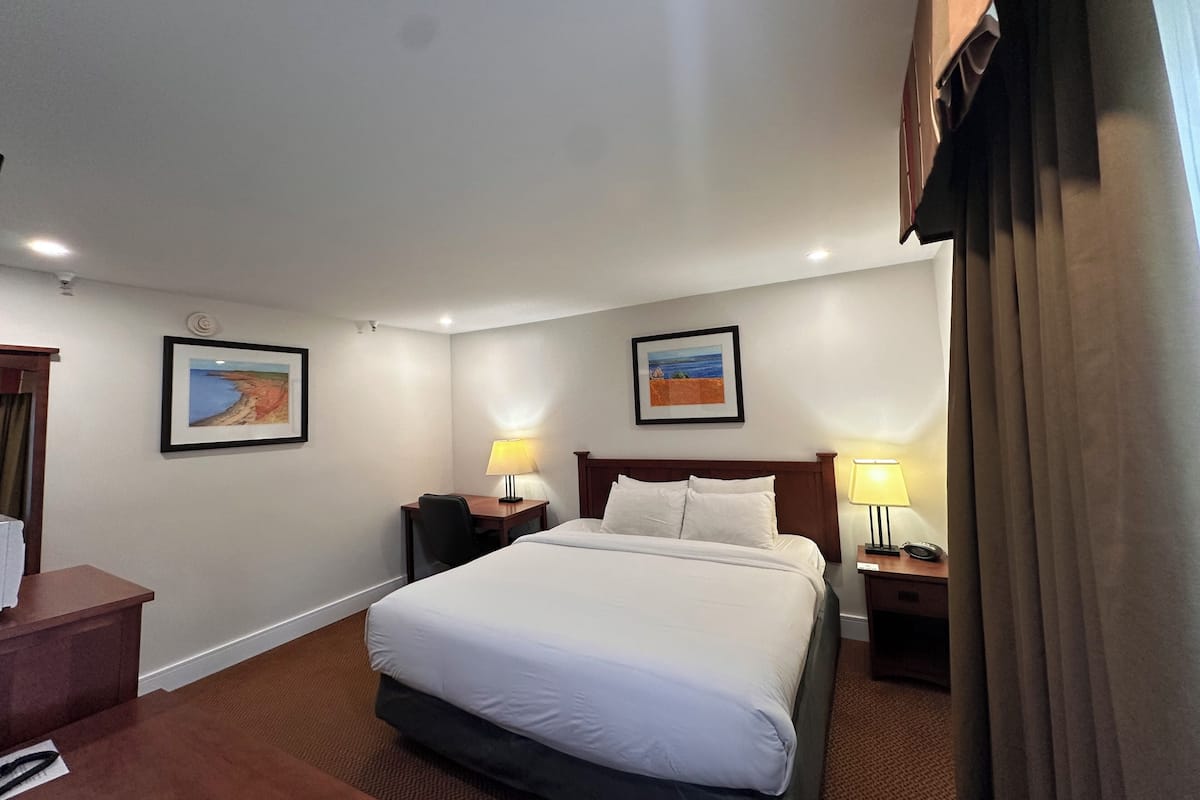 A hotel room with a large bed, two bedside tables with lamps, a desk, and two framed pictures on the walls.