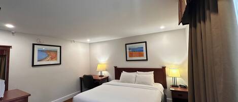 Una habitación de hotel con una cama grande, dos mesitas de noche con lámparas, un escritorio y dos cuadros enmarcados en las paredes.