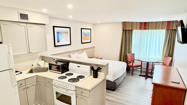 A compact hotel room with a kitchenette, a bed, a small dining area, and a TV mounted on the wall. - Charlottetown Inn & Conference Centre (Charlottetown)