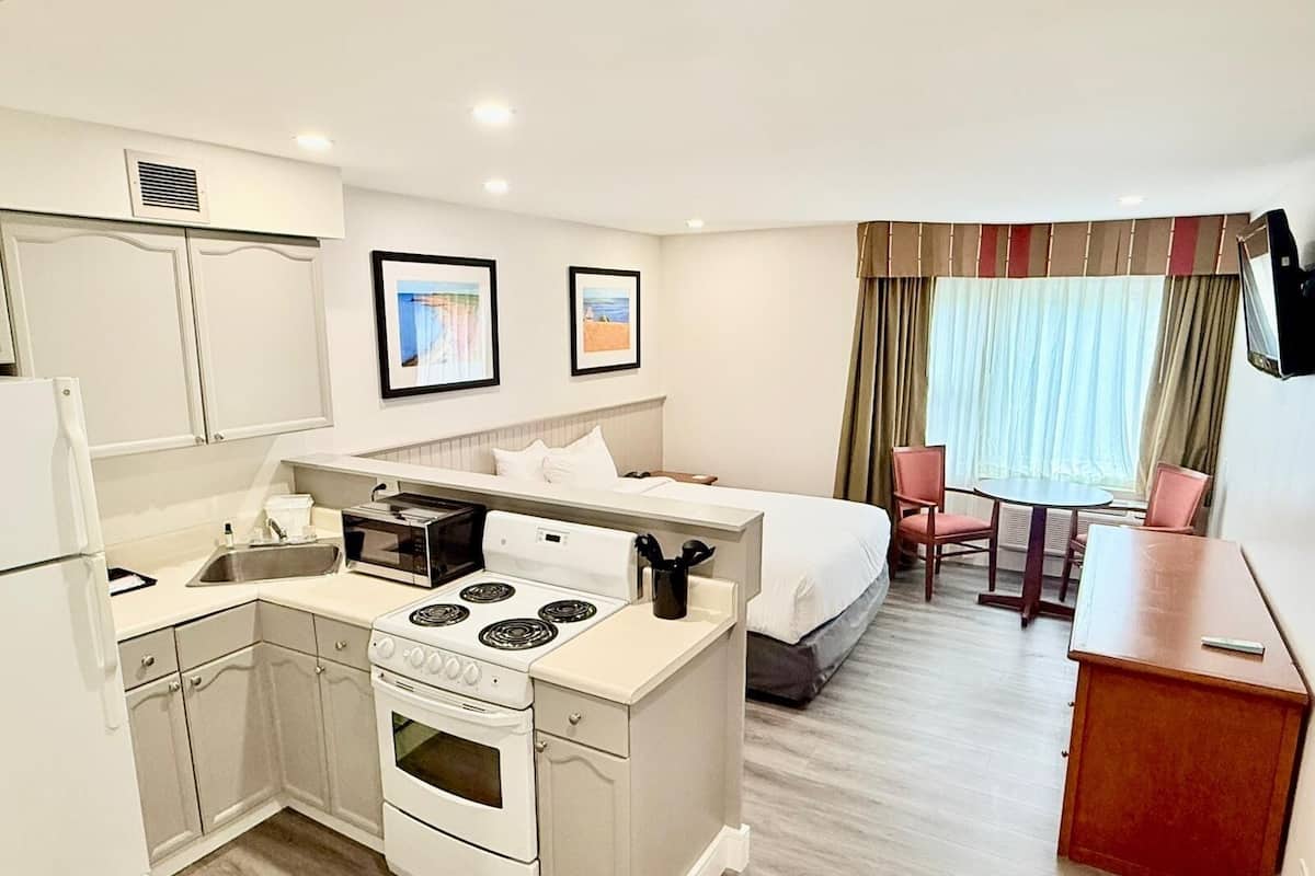 A compact hotel room with a kitchenette, a bed, a small dining area, and a TV mounted on the wall.