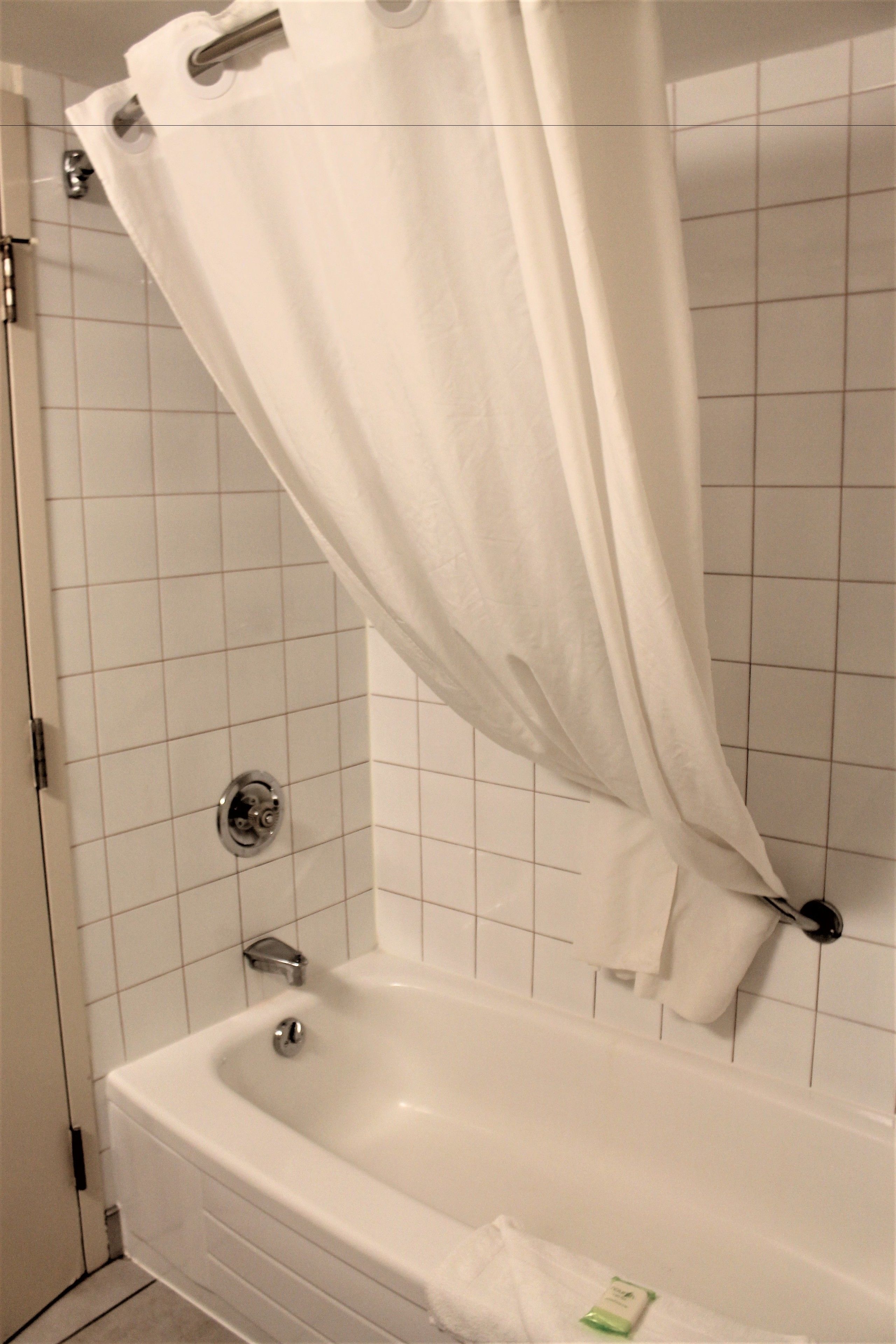 Un baño con una bañera blanca, cortina de ducha y paredes de azulejos.