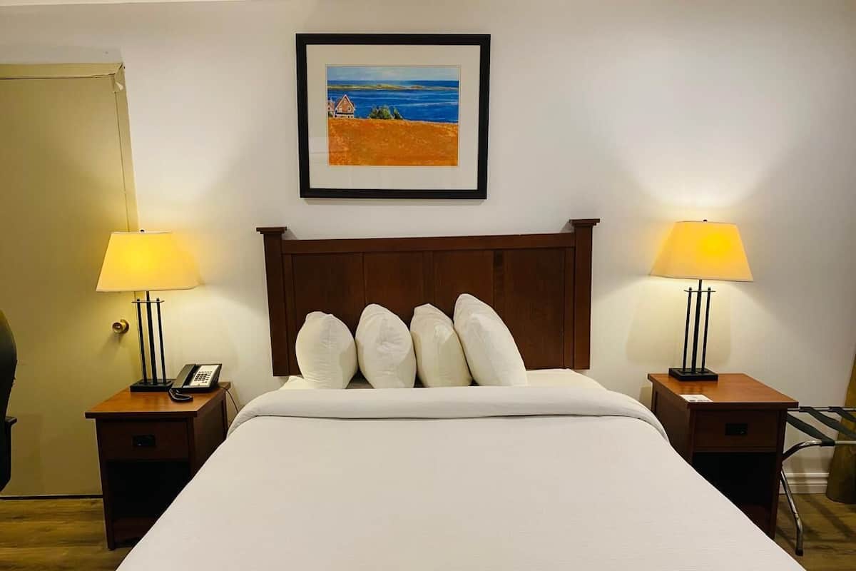 A hotel room with a large bed, two bedside tables with lamps, a framed picture on the wall, and a chair in the corner.
