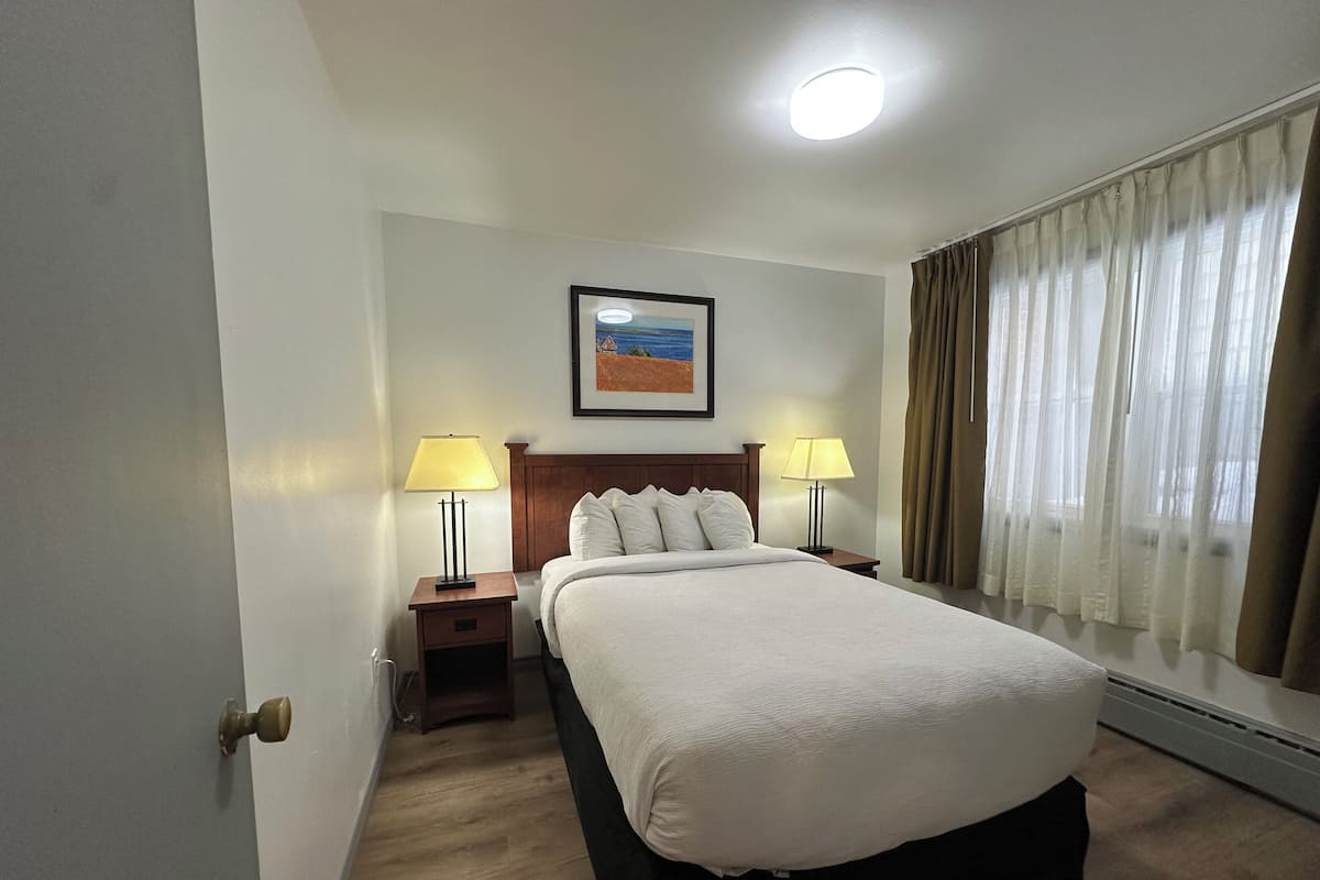 A hotel room with a large bed, two bedside tables with lamps, a framed picture on the wall, and a window with curtains.