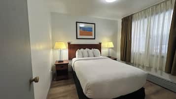 Habitación de hotel con una cama grande, dos mesitas de noche con lámparas, un cuadro en la pared y una ventana con cortinas.