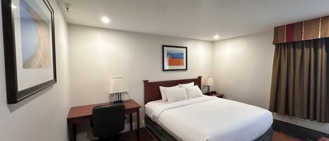 Une chambre d’hôtel avec un lit, deux tables de chevet avec des lampes, un bureau avec une chaise, un tableau encadré au mur et une fenêtre avec des rideaux.