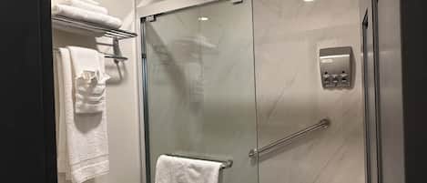 Une salle de bain moderne avec une douche à parois de verre, des toilettes et un porte-serviettes avec des serviettes pliées.