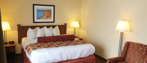 Quarto de hotel com uma cama, duas luminárias de cabeceira, um quadro na parede e uma poltrona estampada.