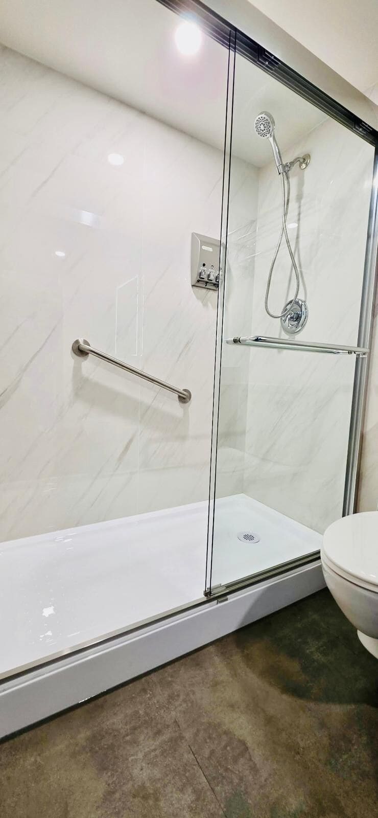 A glass-enclosed shower with a handheld showerhead, a handheld showerhead, and a glass door.