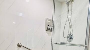 A glass-enclosed shower with a handheld showerhead, a handheld showerhead, and a glass door.