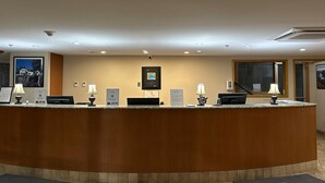 A reception desk with a wooden counter, two lamps, a digital display, and a framed picture on the wall. - Charlottetown Inn & Conference Centre (Charlottetown)