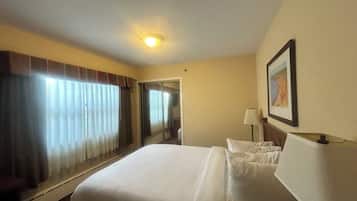 A hotel room with a large bed, a bedside table with a lamp, a framed picture on the wall, and a window with curtains.