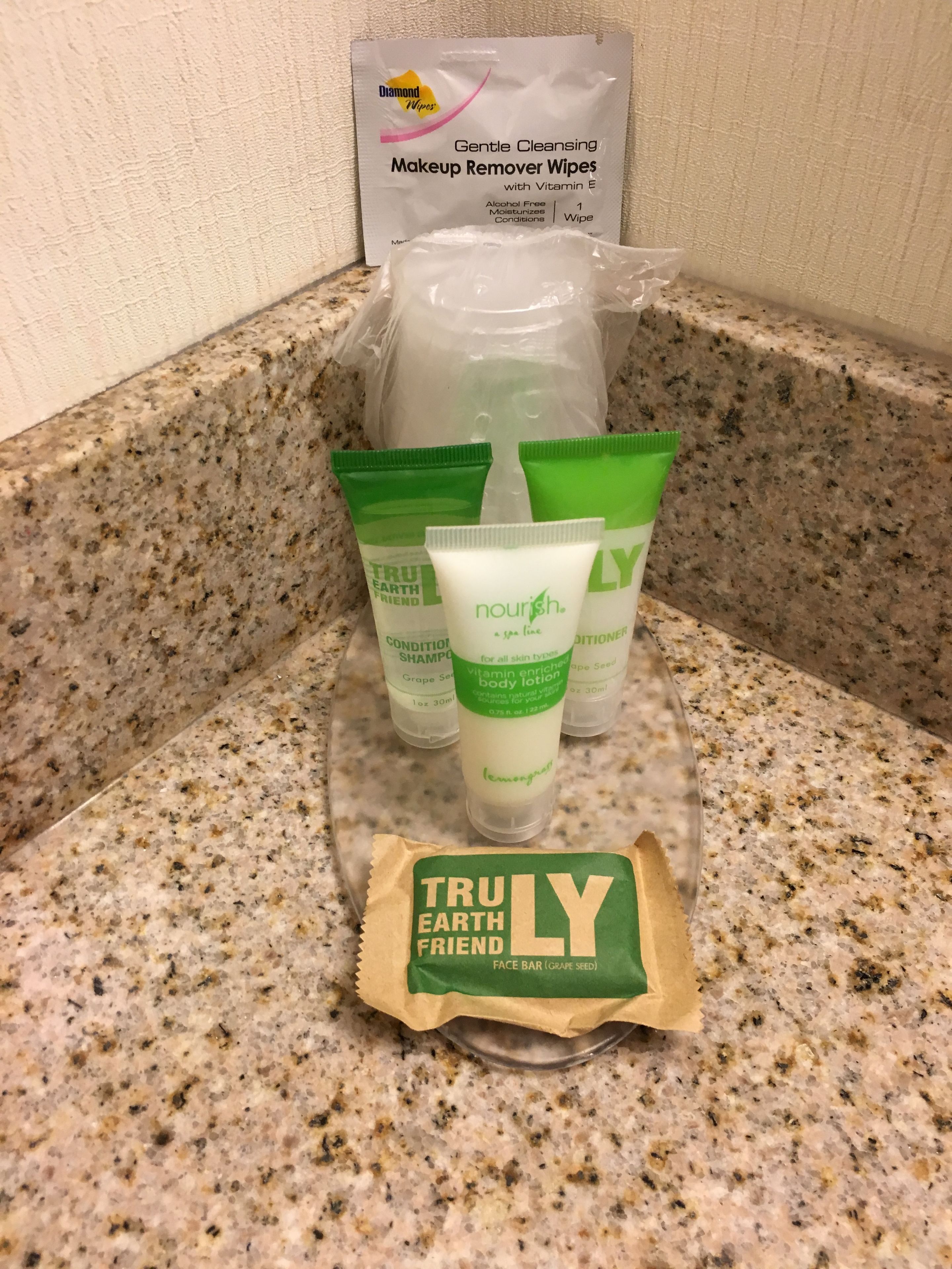 A countertop with a package of Truly Earth Friend face bar (grape seed), a bottle of Diamond wipes makeup remover wipes, and several tubes of Nourish body lotion.