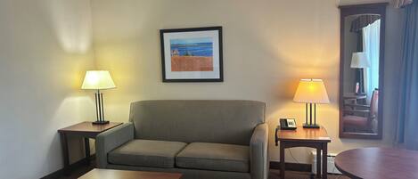 A hotel room with a sofa, two side tables with lamps, a small table, and a framed picture on the wall.