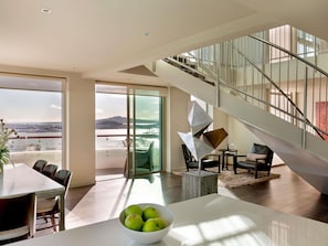 Uma sala de estar moderna com área de jantar, escada e vista para um corpo de água.