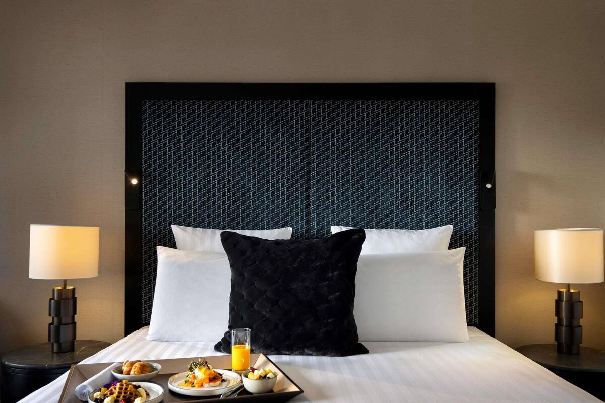 A hotel room with a large bed, two bedside lamps, a tray with breakfast, and a patterned headboard.