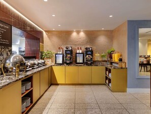 A breakfast bar with a coffee machine, a food display, and a sign listing breakfast specials.
