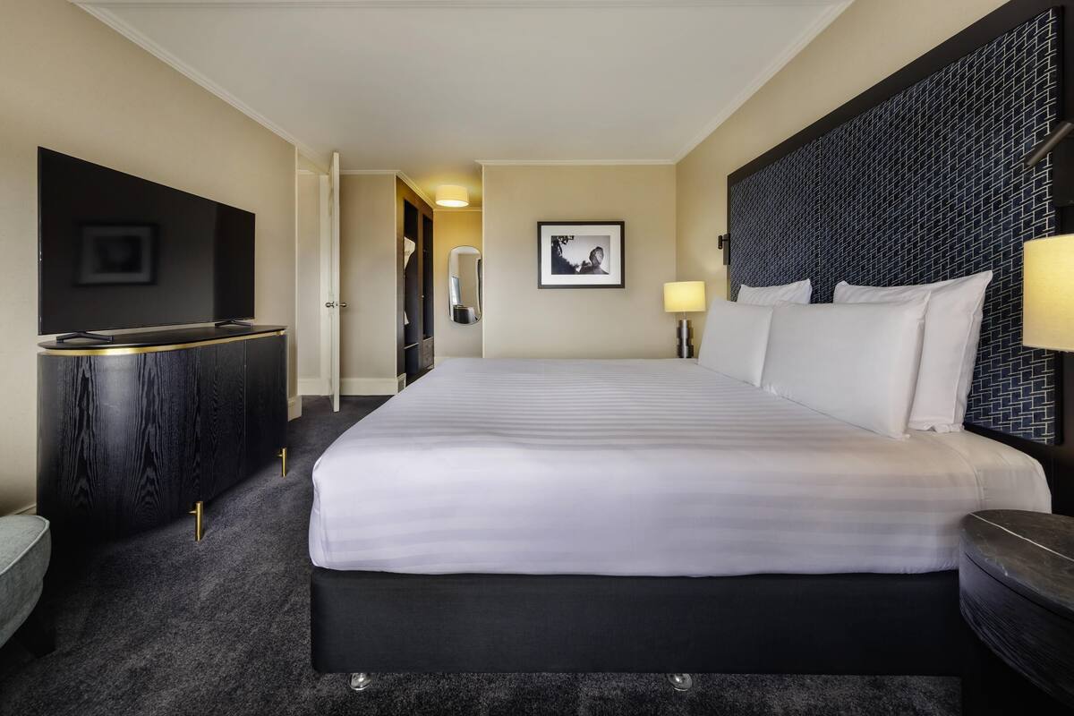 A hotel room with a large bed, a desk, a wardrobe, and a television.