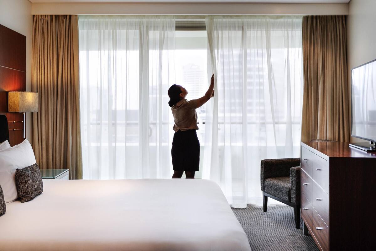 A hotel room with a bed, a desk, a chair, and a large window with curtains.