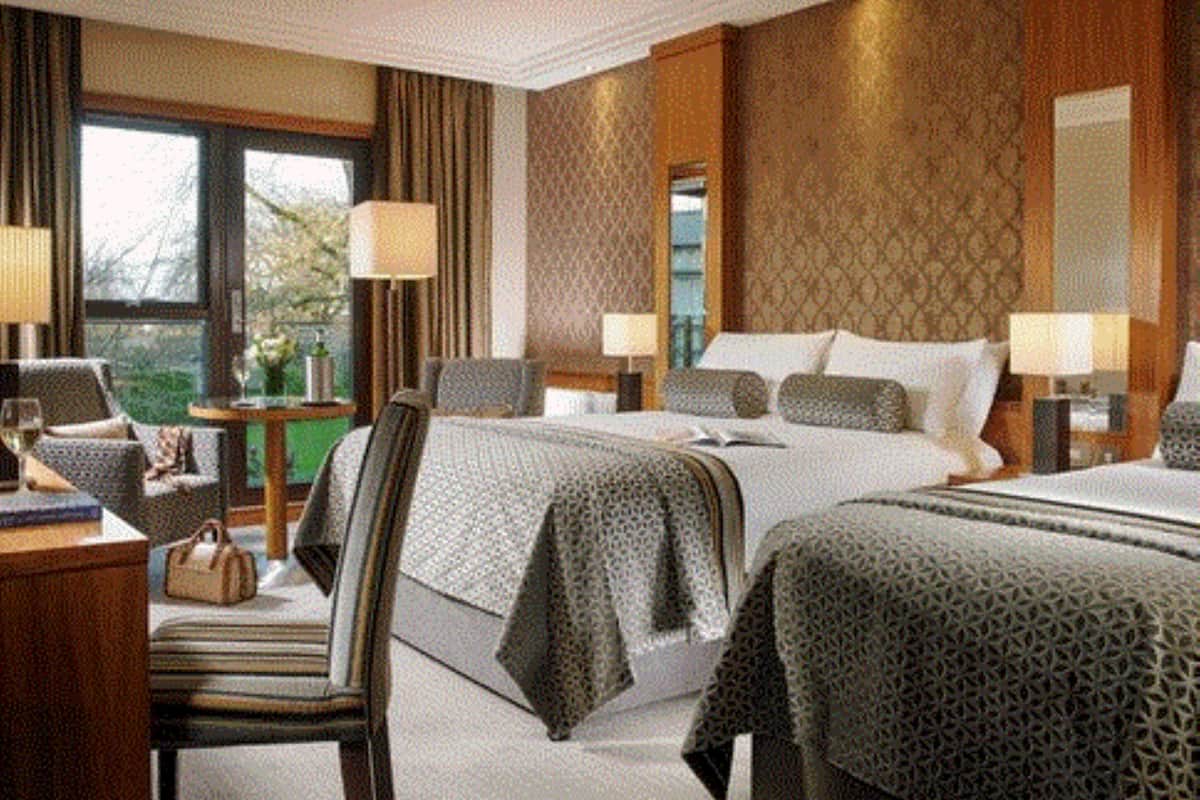 Habitación de hotel con dos camas, un escritorio y una silla. Hay lámparas a ambos lados de las camas y una ventana con cortinas.