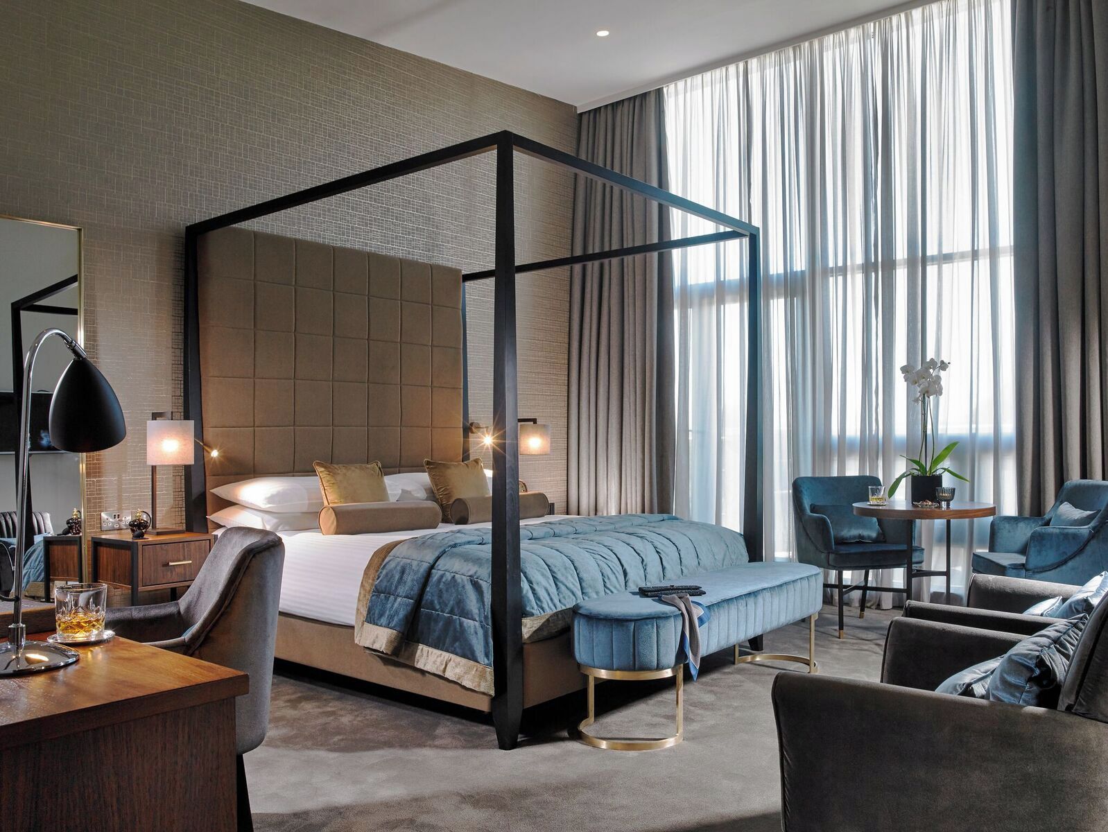 Una habitación de hotel moderna con una cama con dosel, un área de descanso con una mesa redonda y un gran ventanal con cortinas.