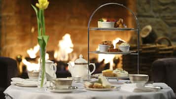 A table set for afternoon tea with a tiered tray, teapot, cups, and a vase of flowers.