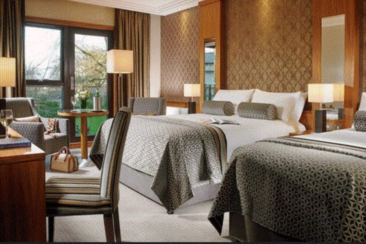 Una habitación de hotel con dos camas, un escritorio, una silla y una ventana con cortinas.