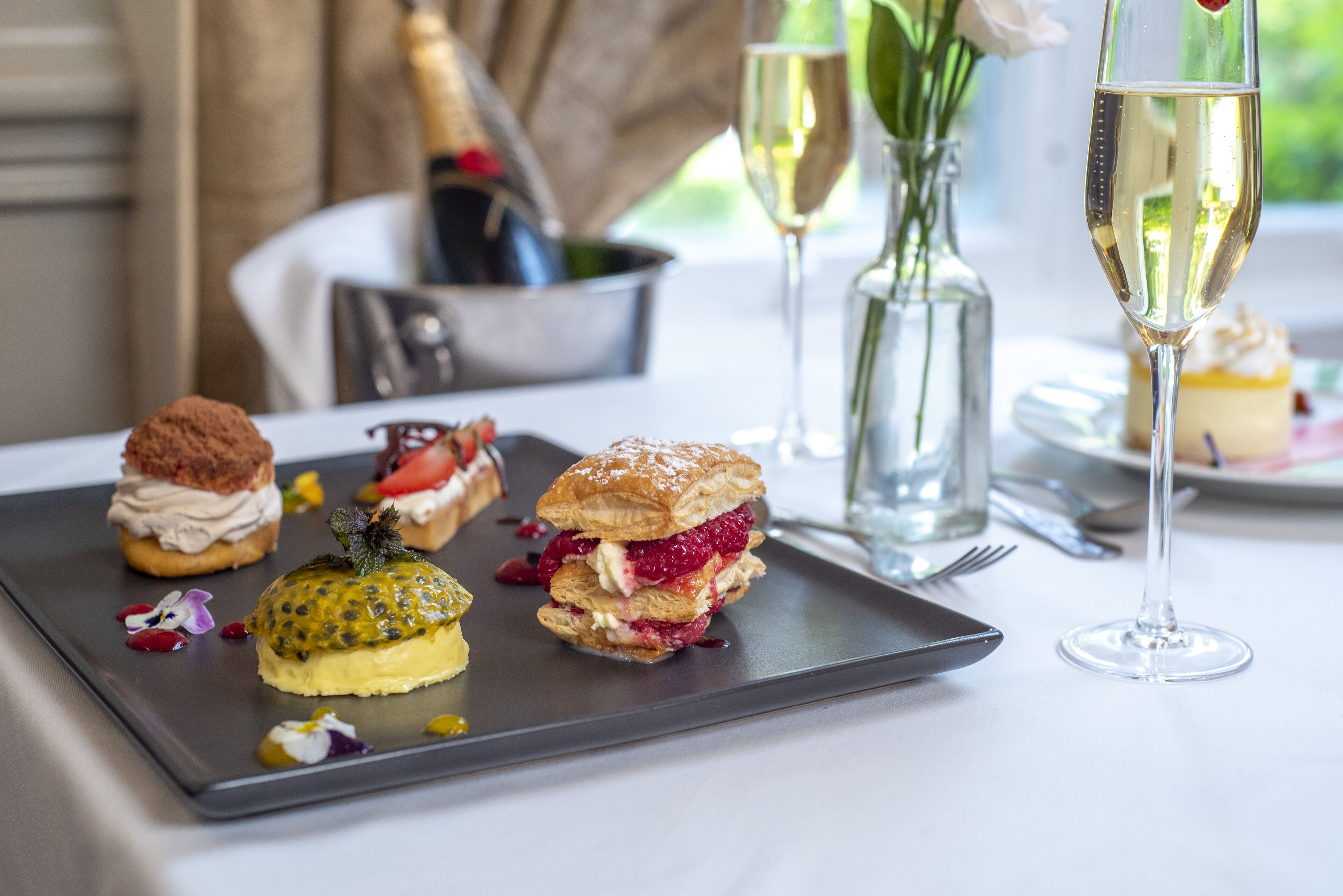 A dessert tray with various pastries and a bottle of champagne on a table.