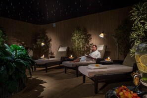 Un espacio de spa con dos sillones reclinables, una mesa con fruta y una bebida, e iluminación ambiental.