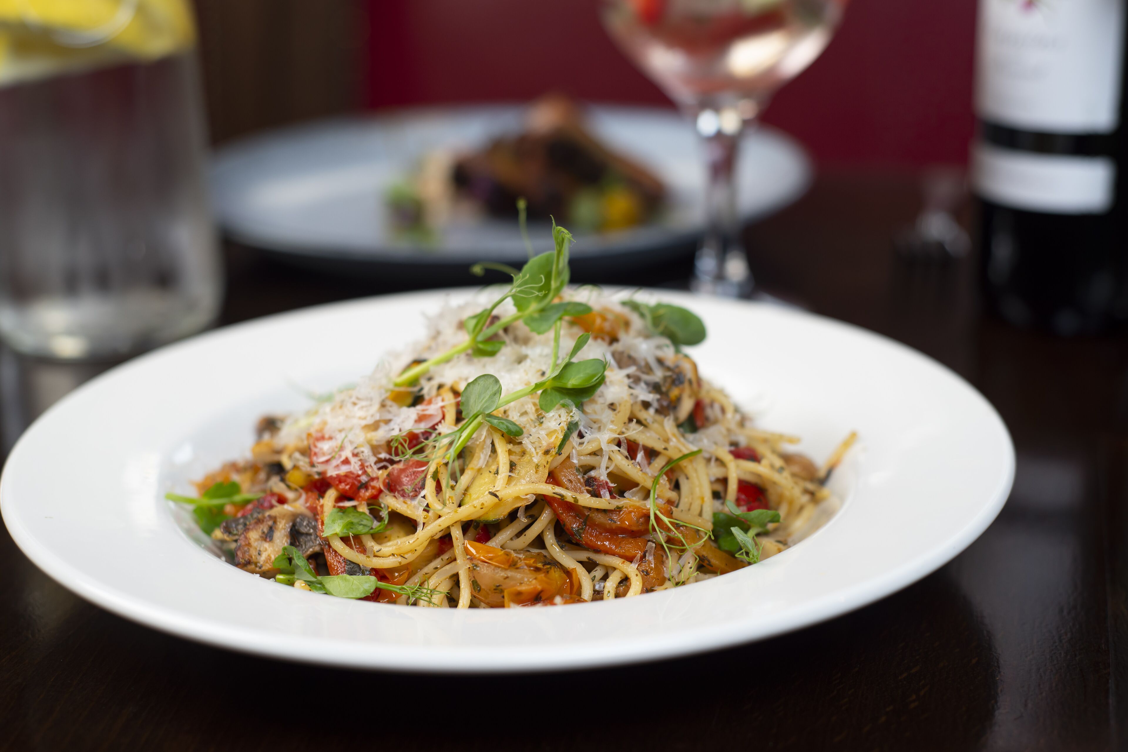 Une assiette de spaghettis avec une sauce tomate, du fromage et des légumes verts.