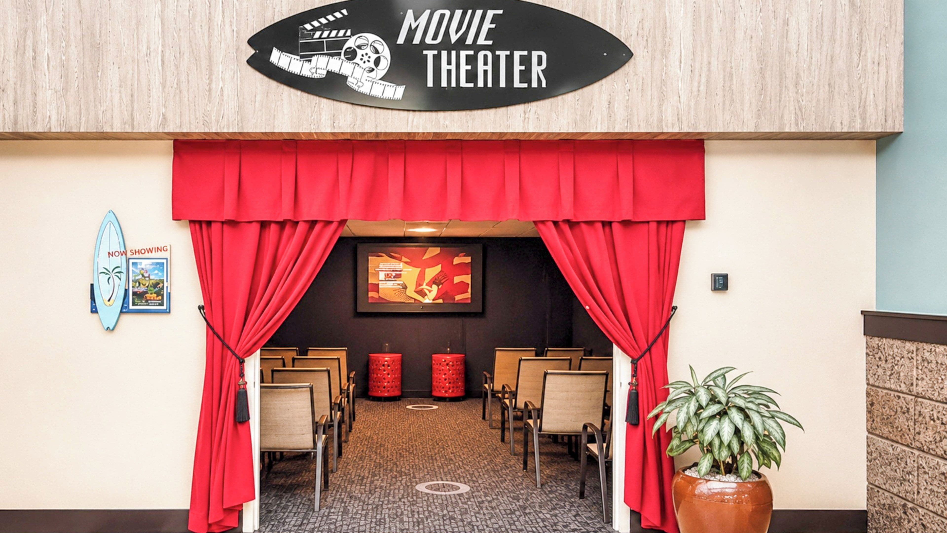 A movie theater entrance with red curtains, a film reel sign, and a poster on the wall.