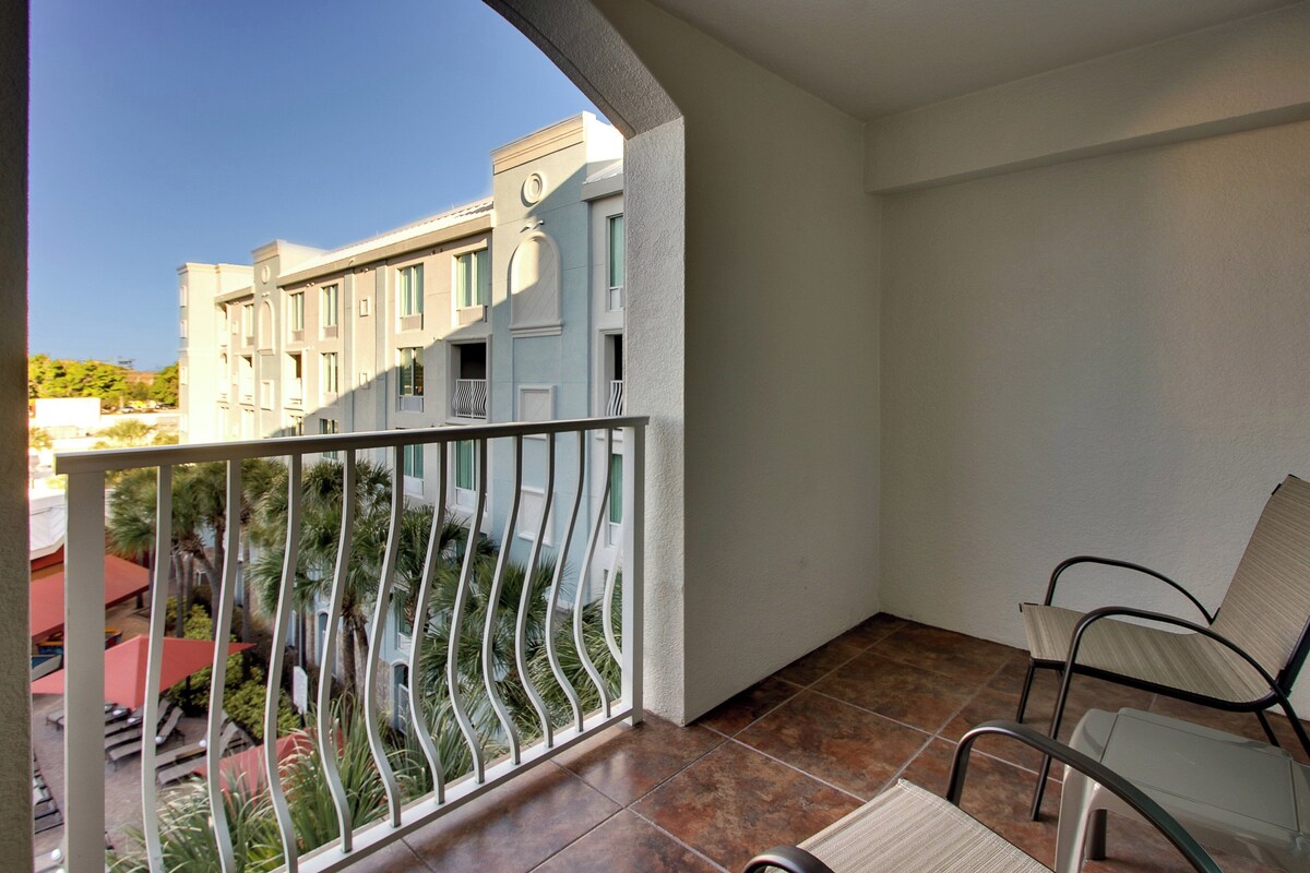 Ein Balkon mit Metallgeländer, einem Stuhl und Blick auf ein Gebäude mit zahlreichen Fenstern und Balkonen.