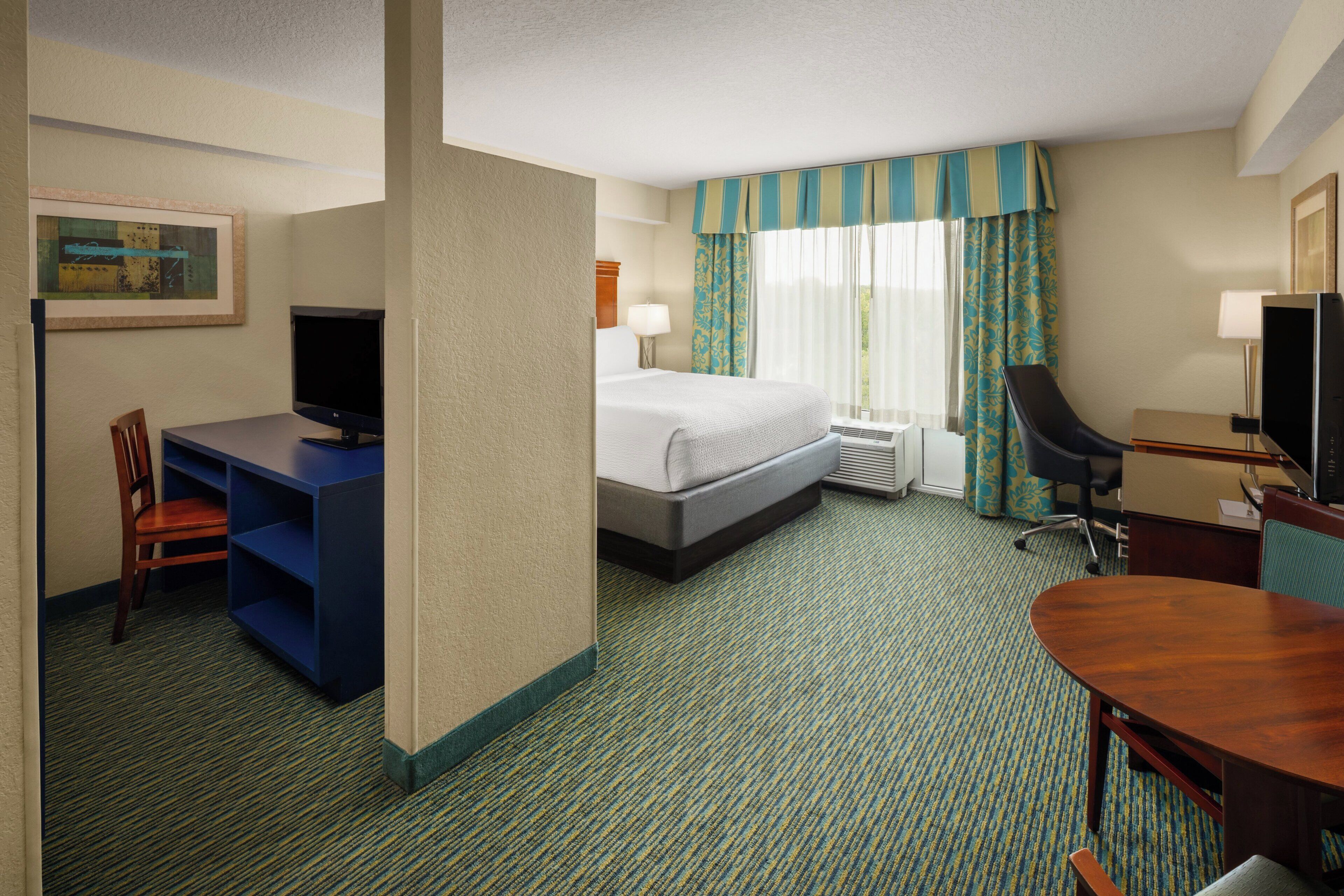 A hotel room with a bed, desk, chair, television, and a painting on the wall.