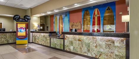 A hotel reception area with a marble counter, a Mickey Mouse decoration, and surfboards on the wall.
