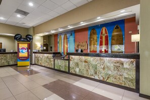 A hotel reception area with a marble counter, a Mickey Mouse decoration, and surfboards on the wall. - Holiday Inn Resort Orlando - Lake Buena Vista by IHG (Orlando)