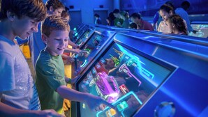 A group of people playing arcade games in a brightly lit room with multiple gaming stations.