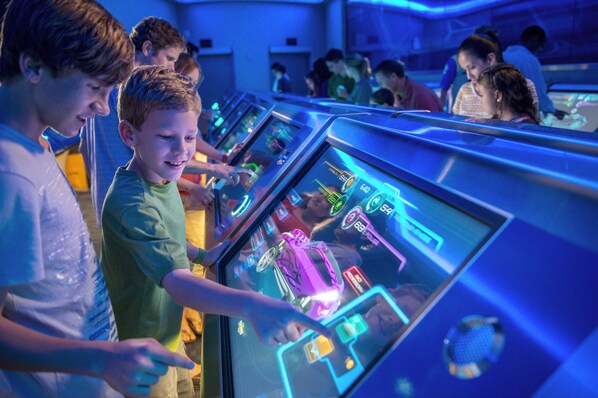 Un grupo de personas jugando videojuegos en un espacio iluminado con varias estaciones de juego.